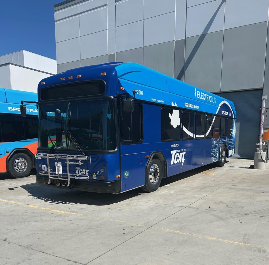 Długi elektryczny autobus pokonuje podmiejską trasę wśród pól i lasów o zachodzie słońca